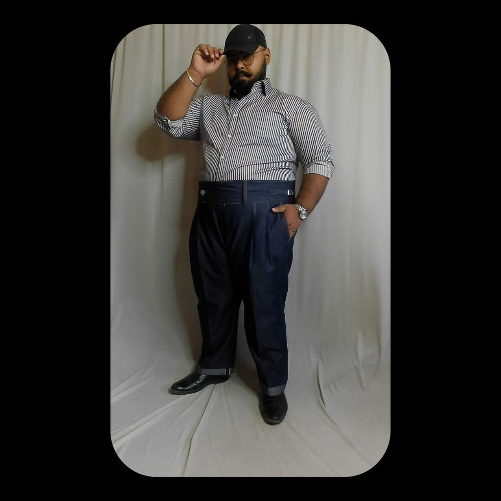 Man posing against a white backdrop wearing a blue striped shirt and dark pants.
