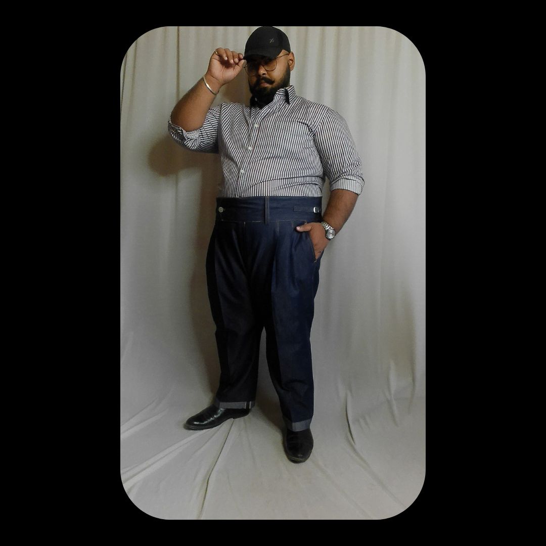 Man posing against a white backdrop wearing a blue striped shirt and dark pants.