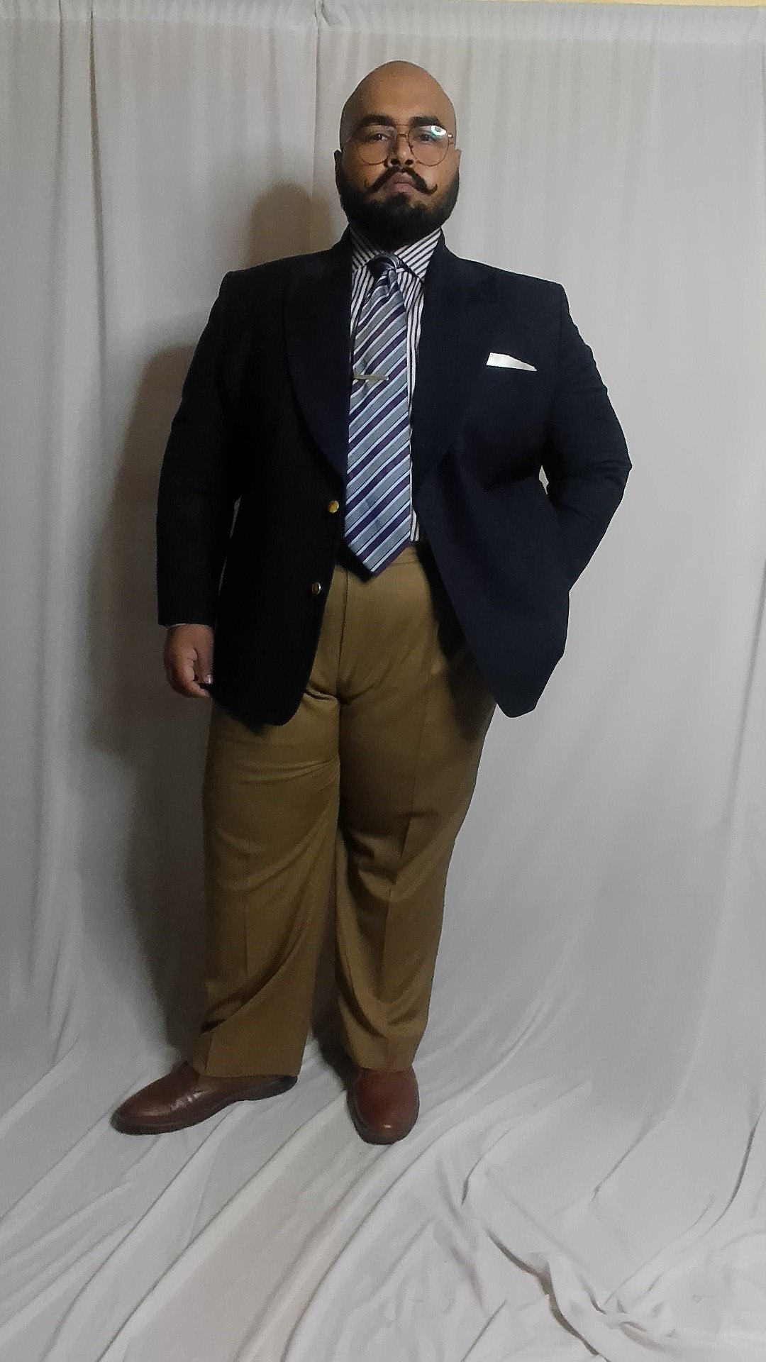 Man wearing a navy suit jacket and striped shirt with khaki pants and striped tie
