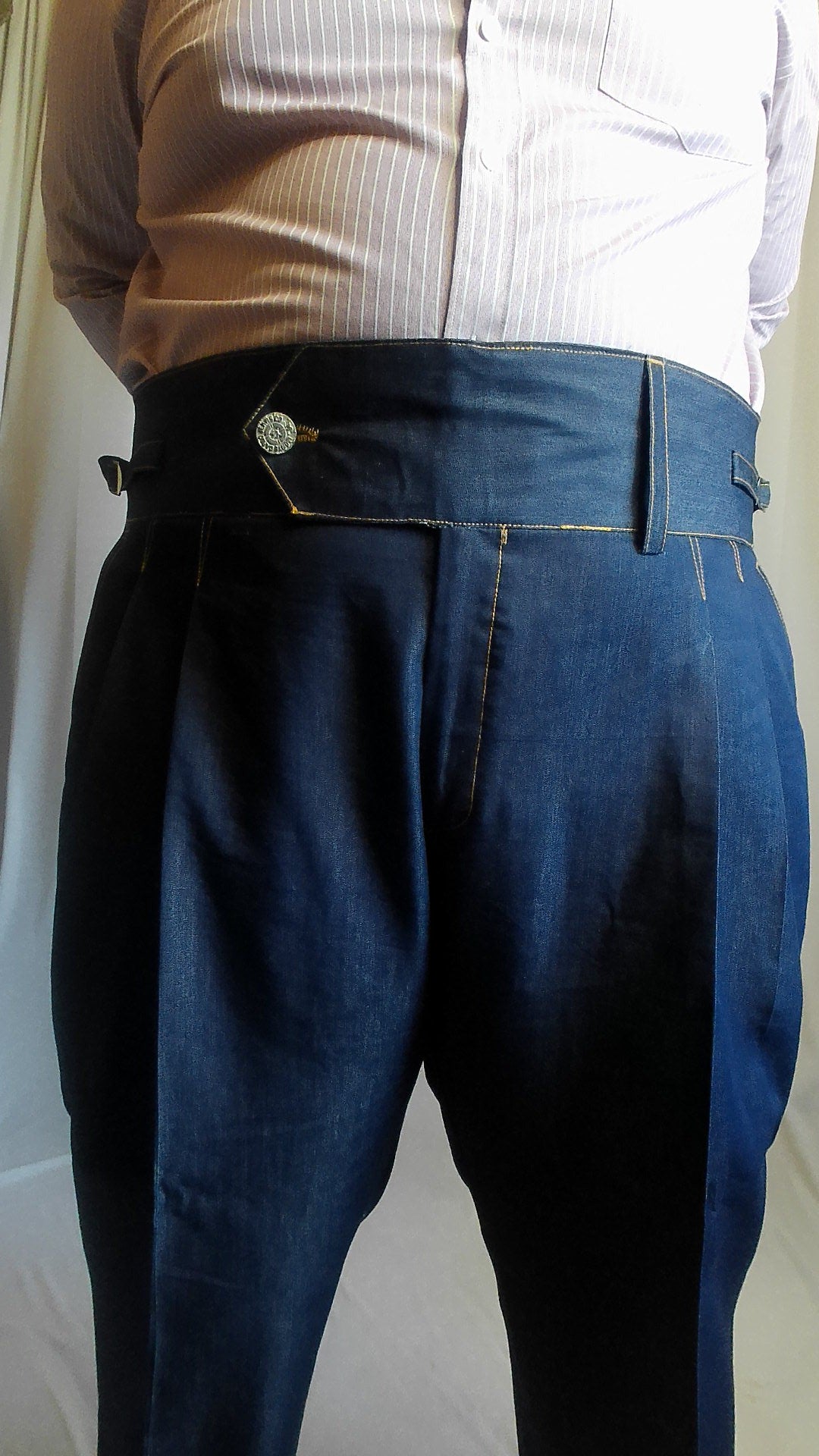 Person wearing dark blue gurkha jeans and a light-colored shirt with a neutral background