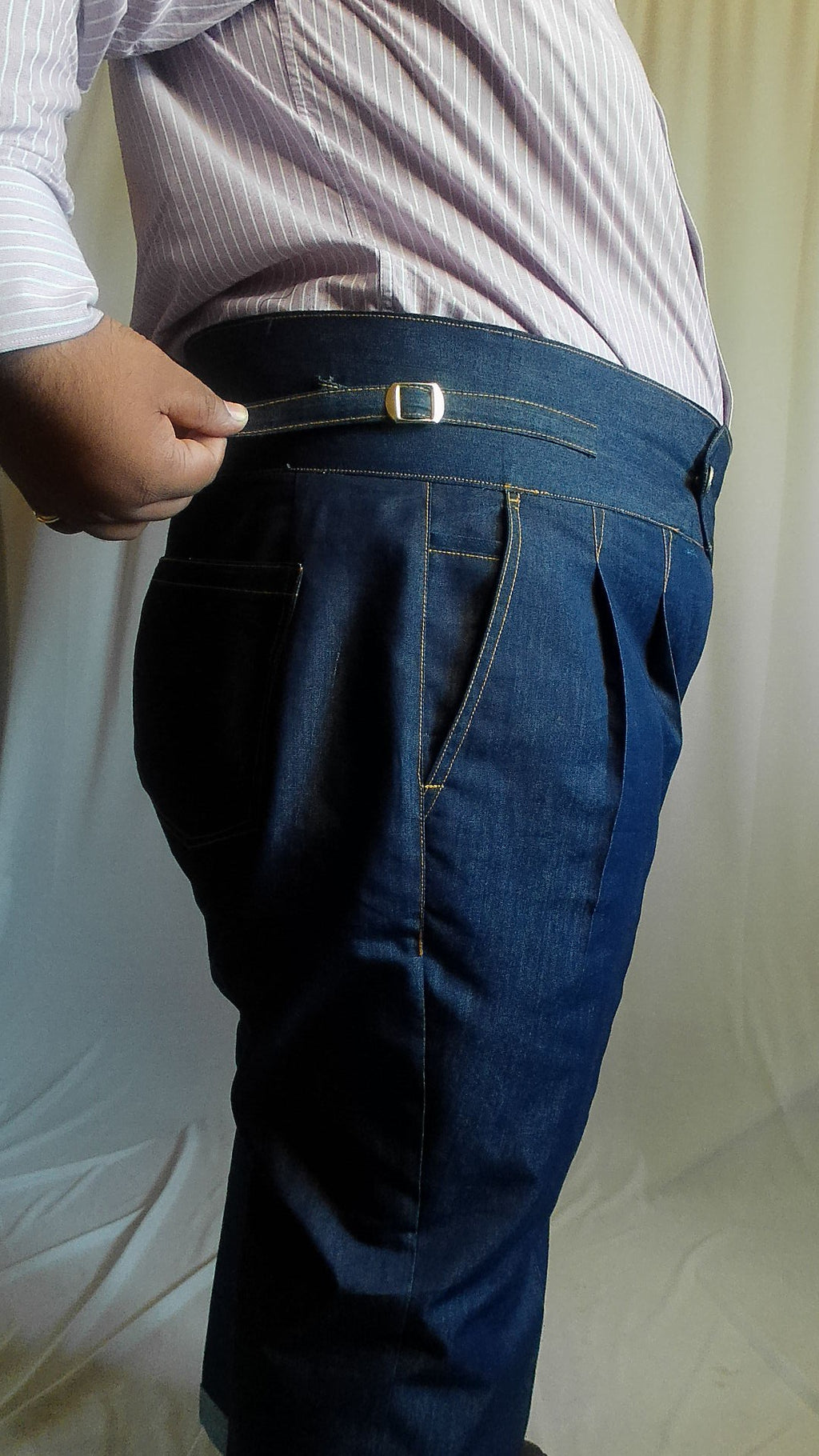Person adjusting a side adjuster on an indigo blue denim trouser against a white background