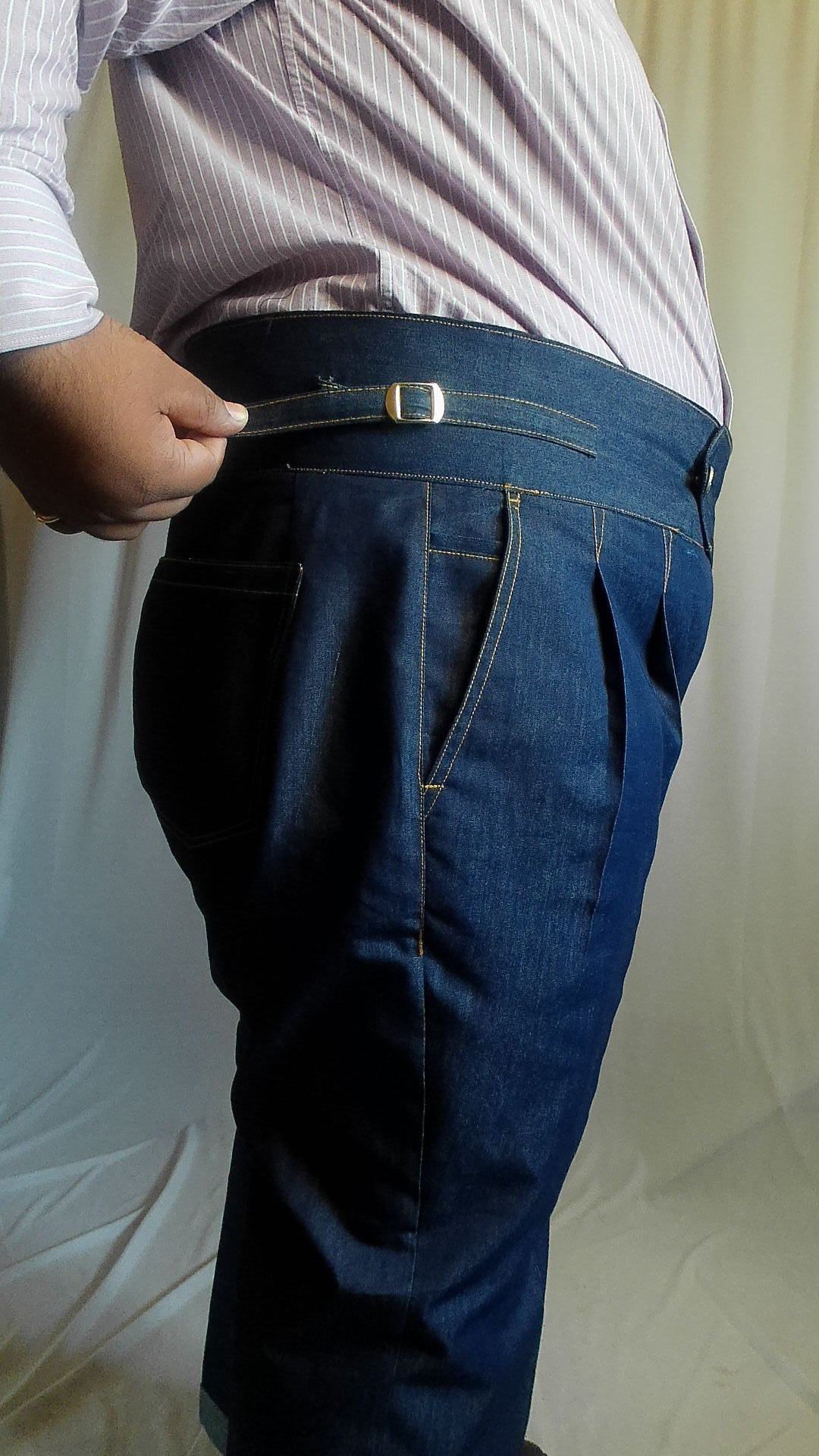Person adjusting a side adjuster on an indigo blue denim trouser against a white background