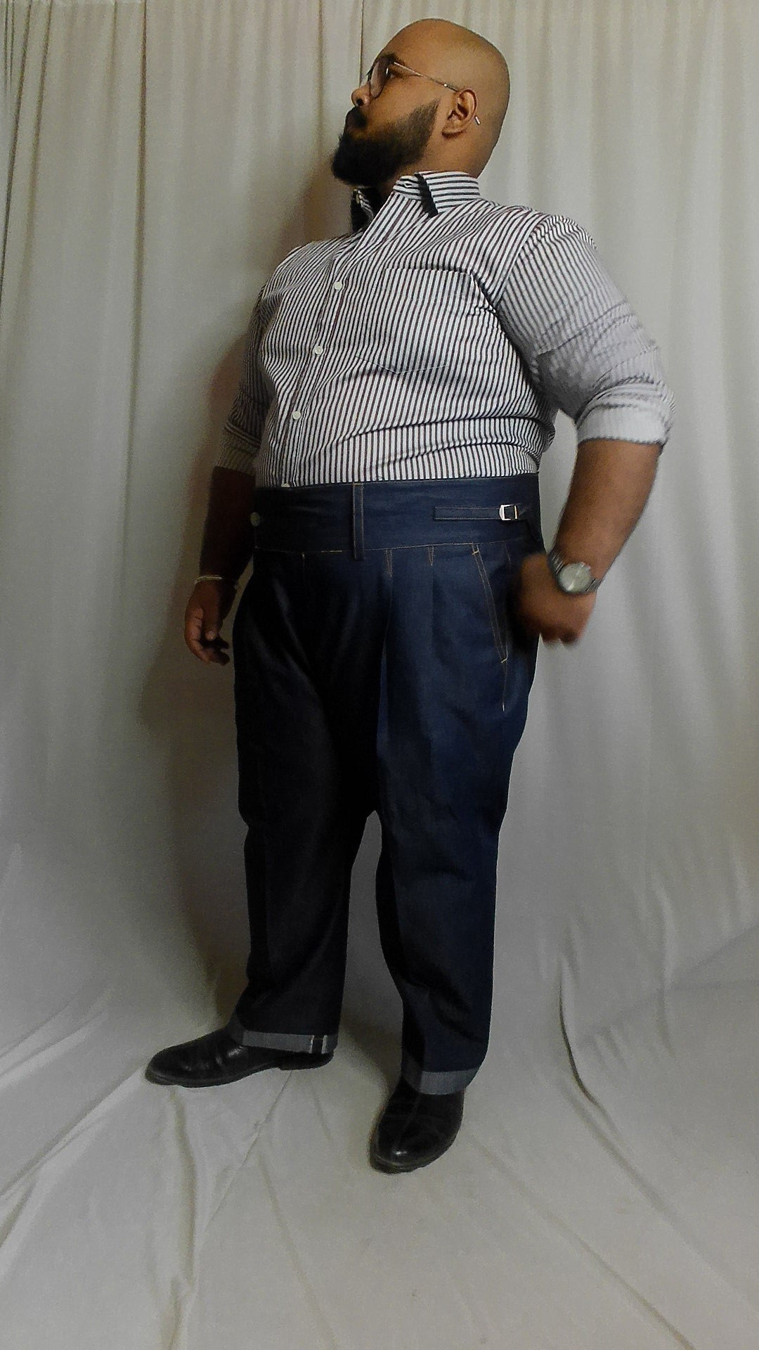 Man wearing a blue pencil striped shirt and blue overalls against a white background